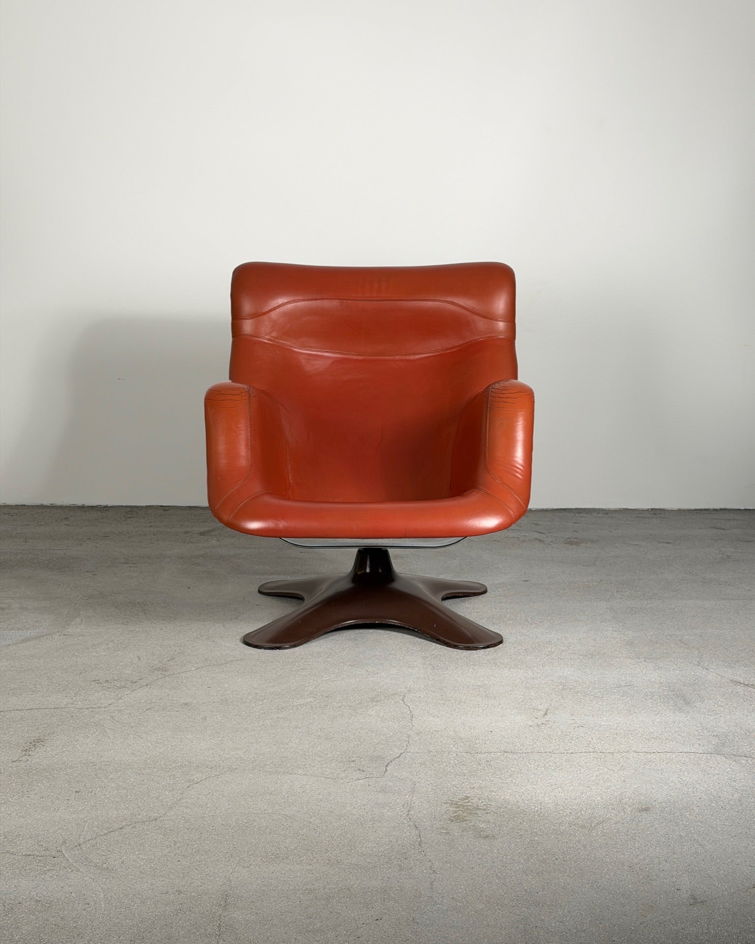Brown leather Karuselli armchair on a gray floor with a white wall background
