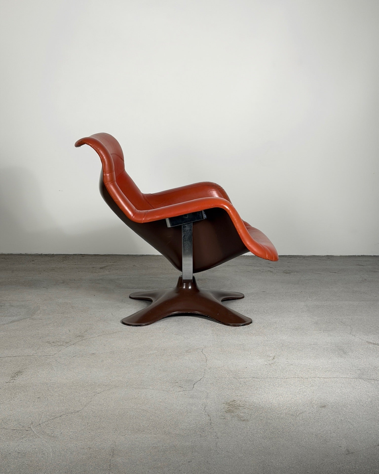 Brown Karuselli chair with a unique design on a gray floor and white wall background
