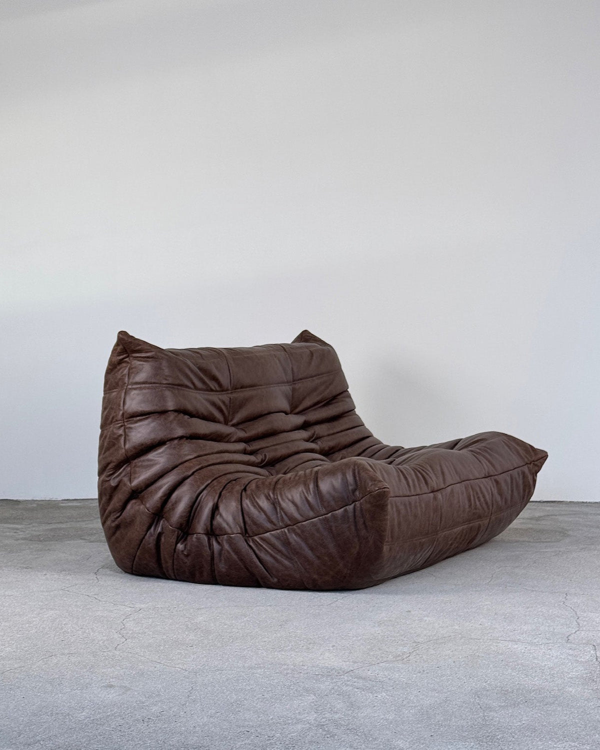 A brown leather 2-seater Togo sofa by Michel Ducaroy for Ligne Roset with a low-profile silhouette and plush, quilted construction.