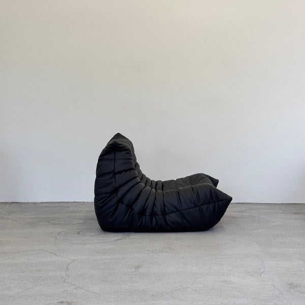 Black togo chair on a gray floor with a white wall background