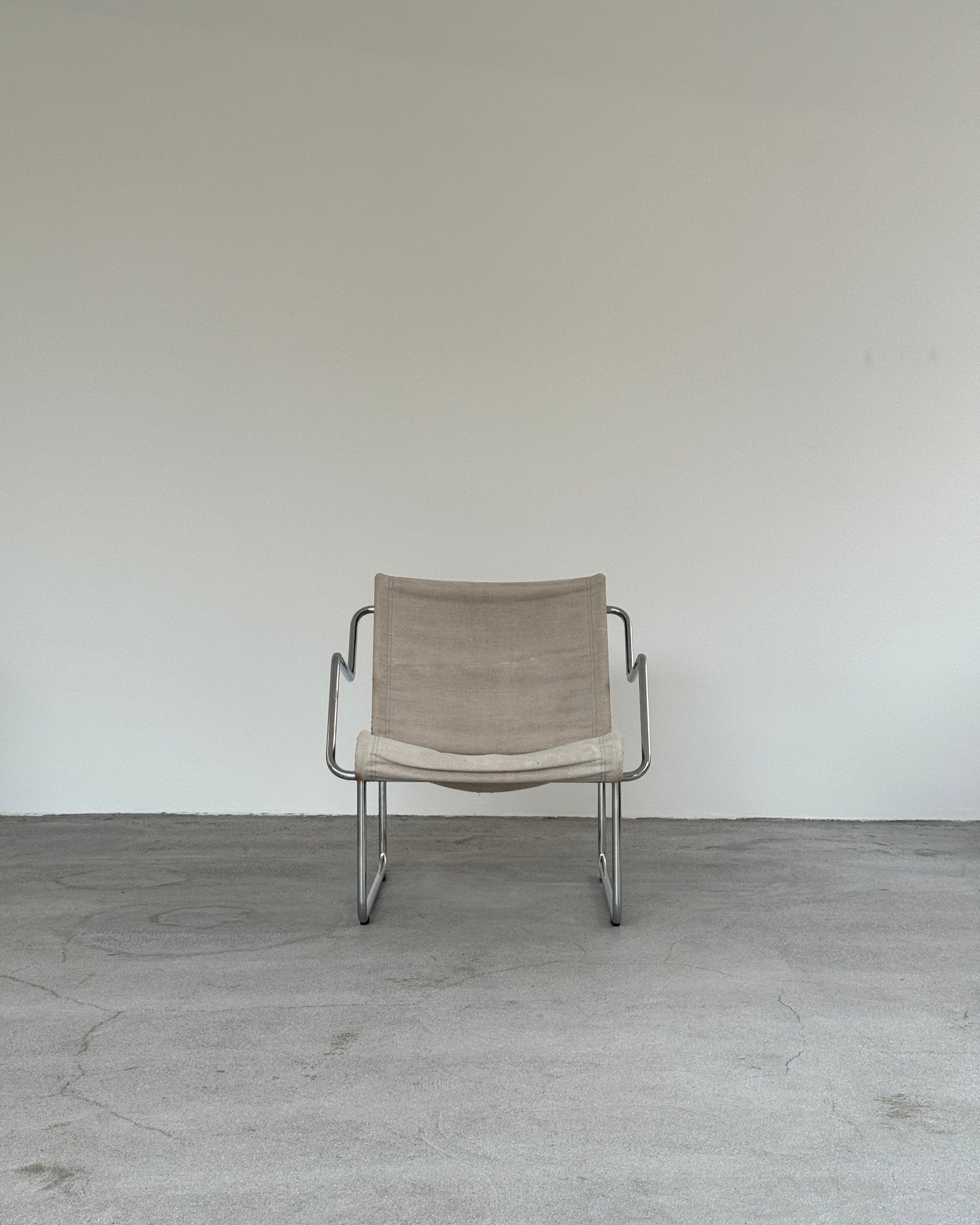 Beige chair with metal frame on a gray floor and white wall