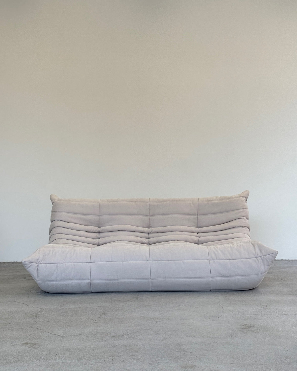 A gray Ligne Roset Togo sofa with a minimalist design and plush, quilted construction, featuring a low-profile silhouette.