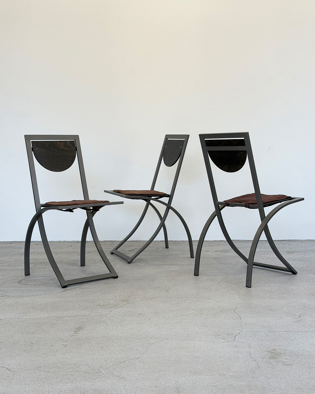 Three modern chairs with metal frames and brown seats on a light wooden floor.