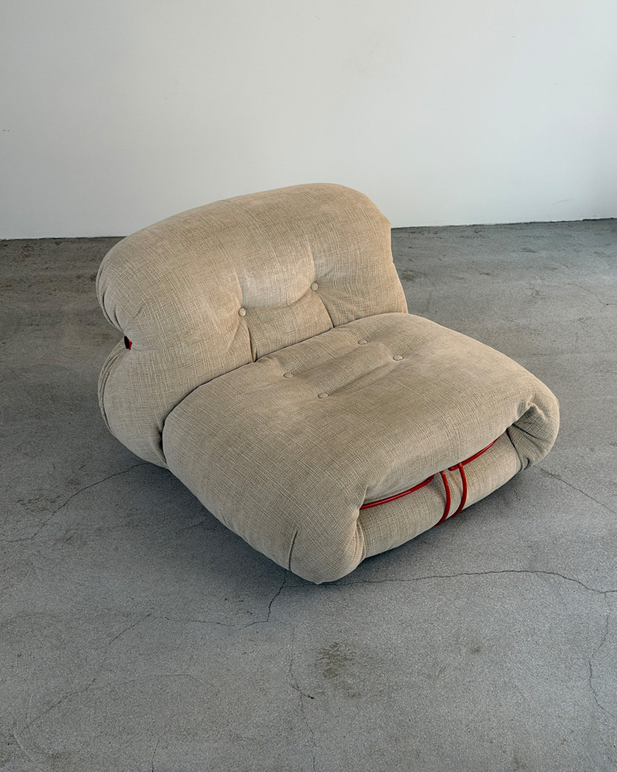 A Beige Soriana Lounge Chair by Afra & Tobia Scarpa for Cassina in a light beige linen fabric, set on a gray concrete floor against a plain white wall.