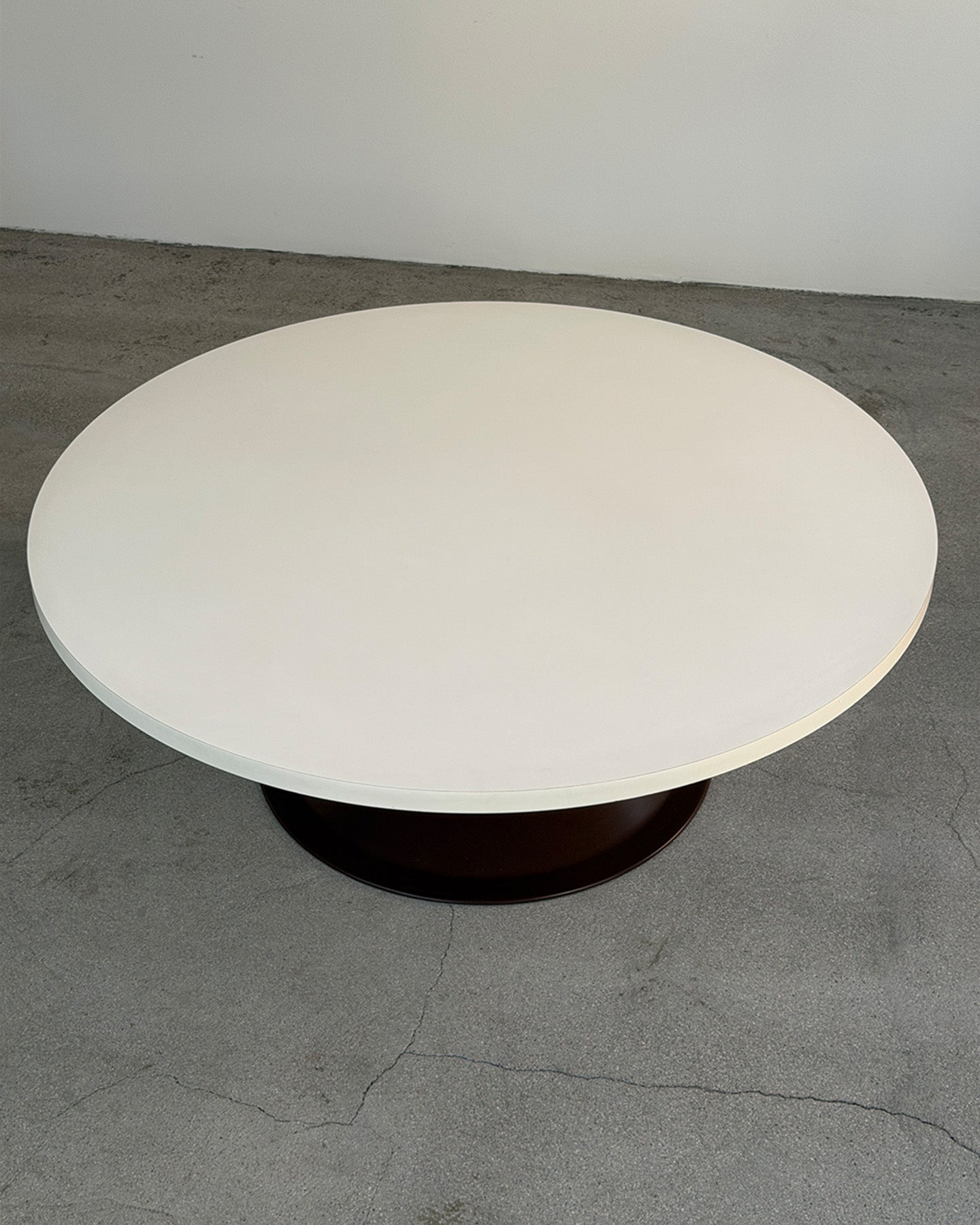 Round white table on a gray floor with a plain white wall background