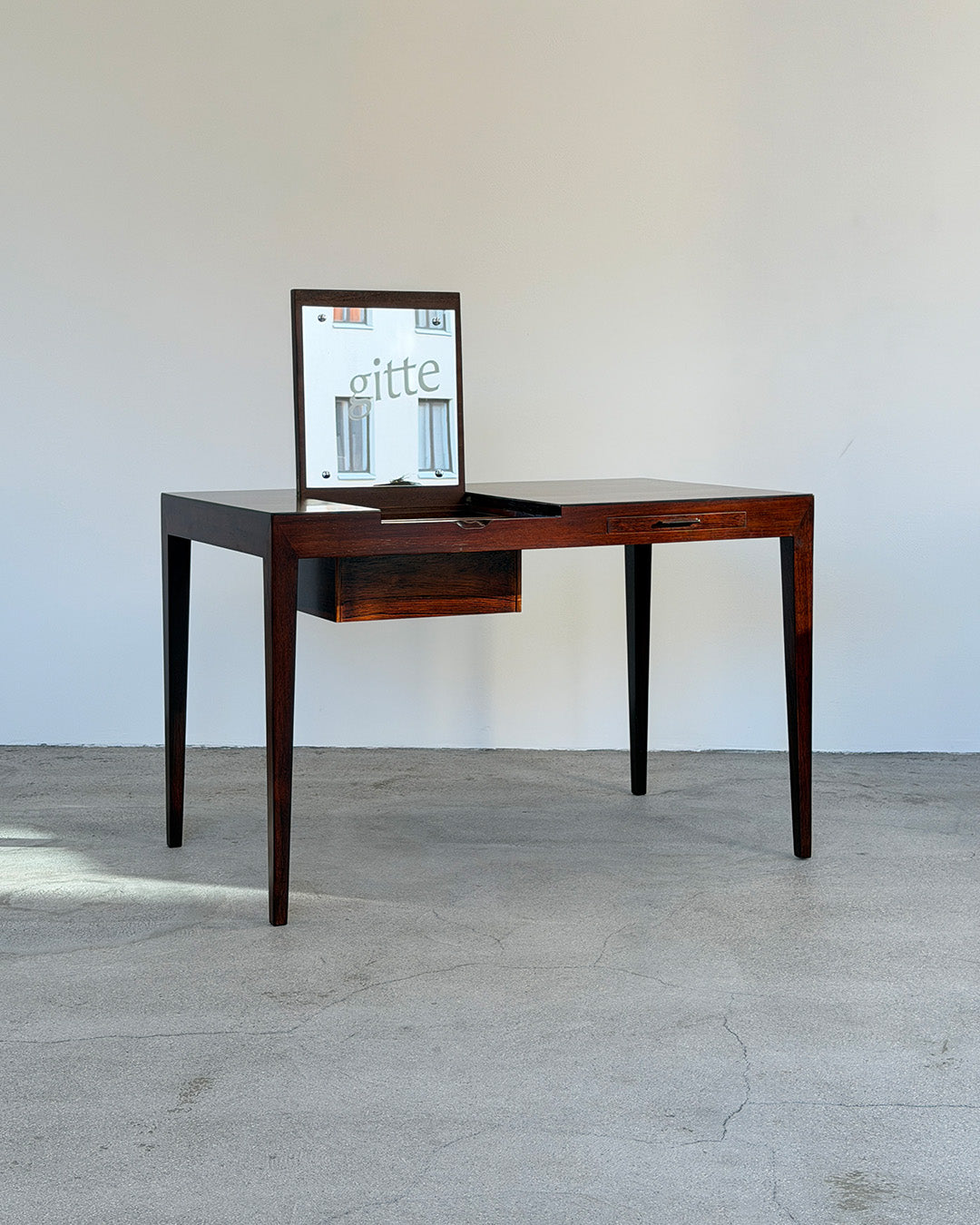 Wooden desk with a mirror on a light gray floor and white wall background
