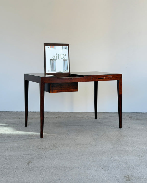 Wooden desk with a mirror on a light gray floor and white wall background