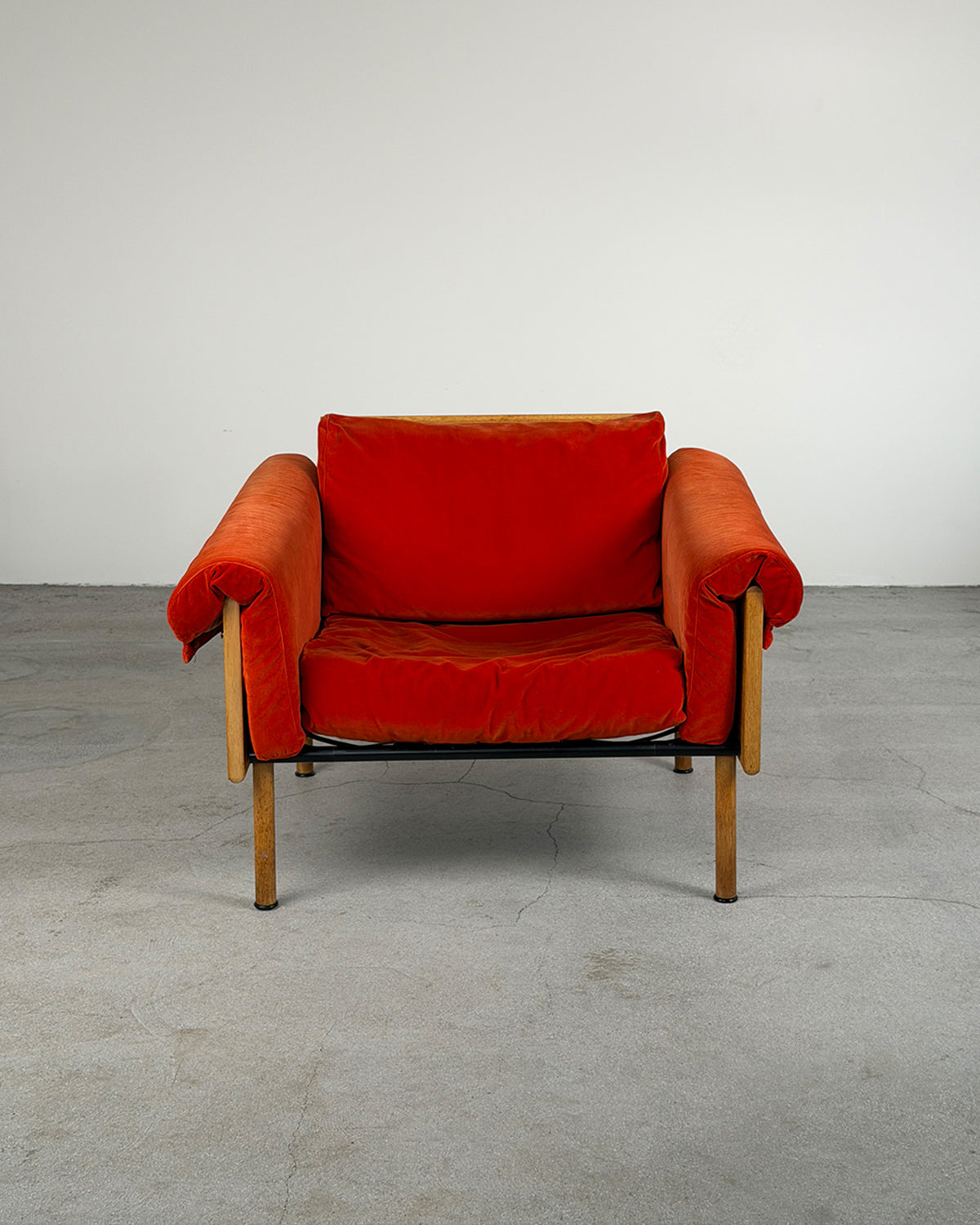Red armchair with wooden frame on a gray floor and white wall background