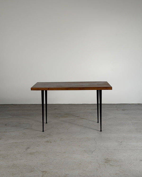 Wooden table with black legs on a gray floor and white wall