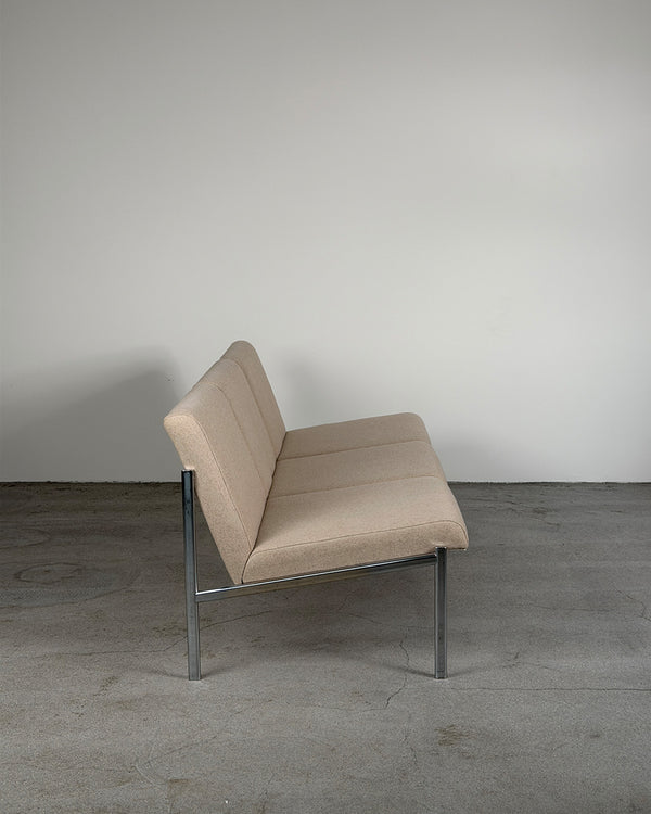 Beige sofa chair with metal frame on a gray floor against a white wall