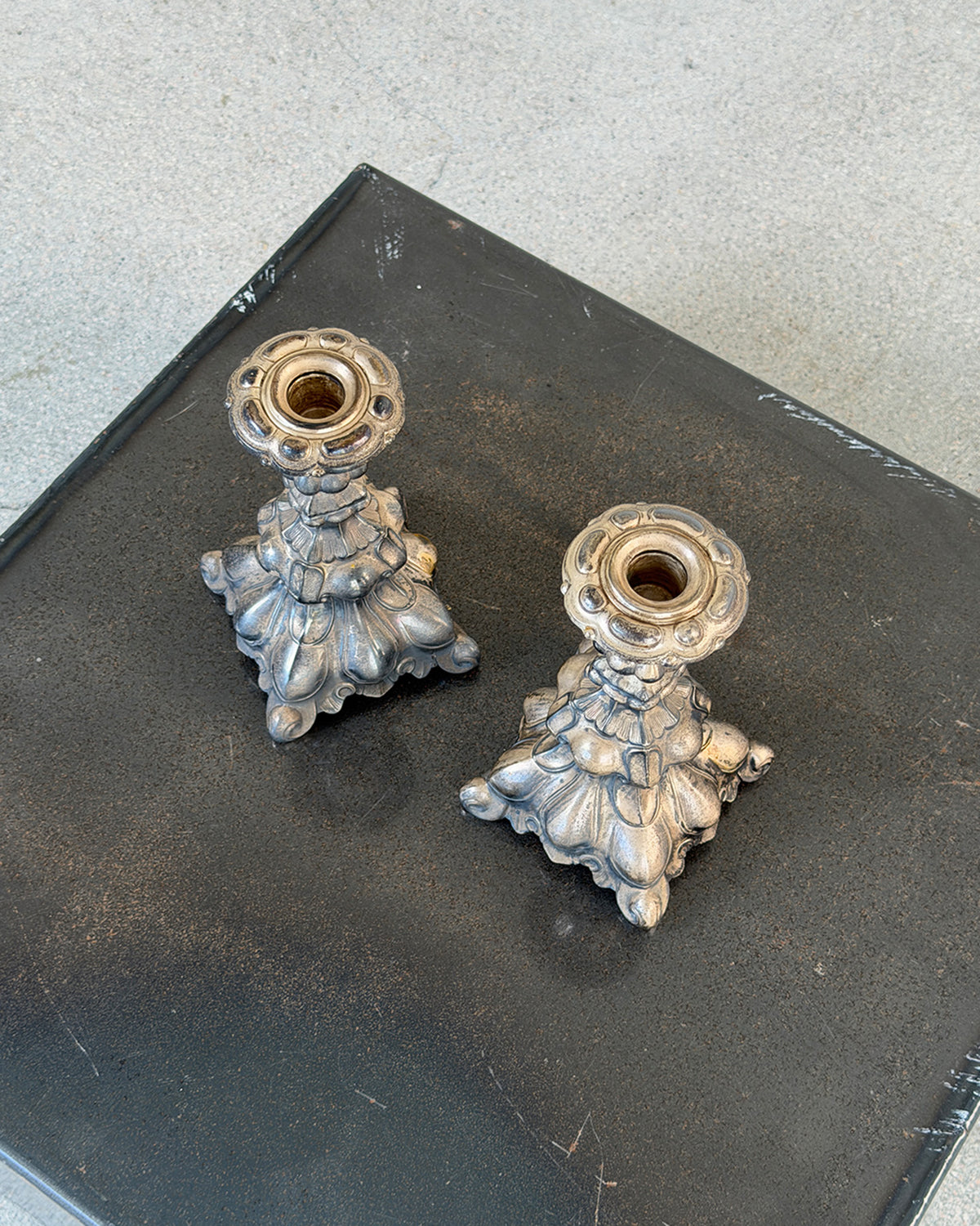 A pair of ornate vintage silver candlestick holders with sculpted floral bases, displayed on a dark gray textured surface.