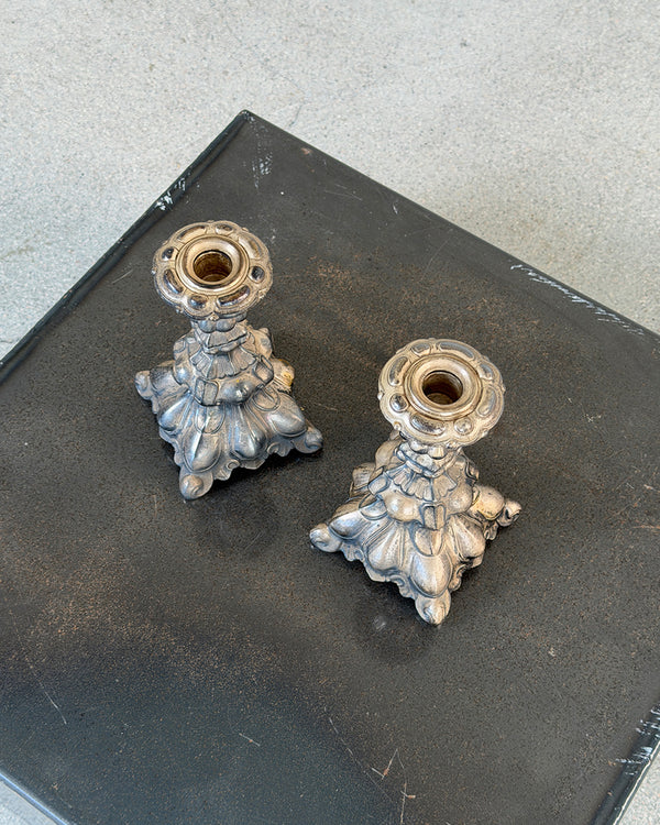 A pair of ornate vintage silver candlestick holders with sculpted floral bases, displayed on a dark gray textured surface.
