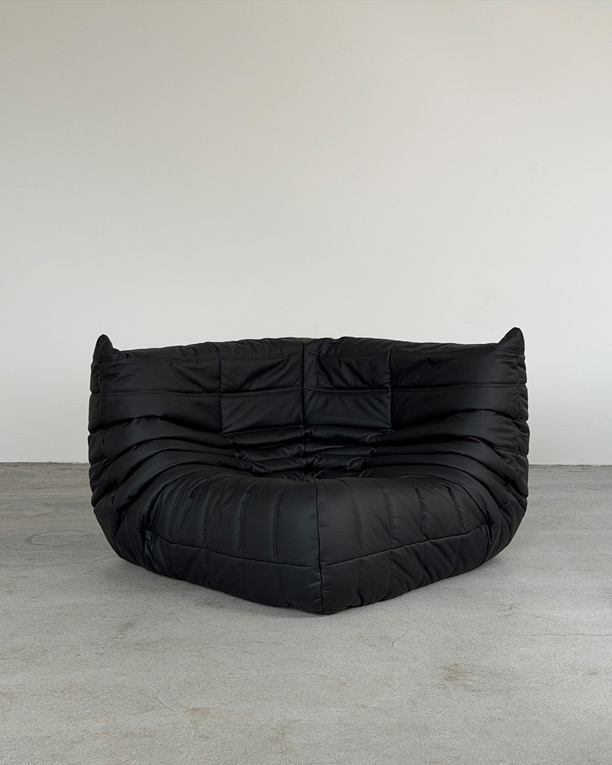 A black leather corner Togo lounge chair by Michel Ducaroy for Ligne Roset, shown on a plain background.