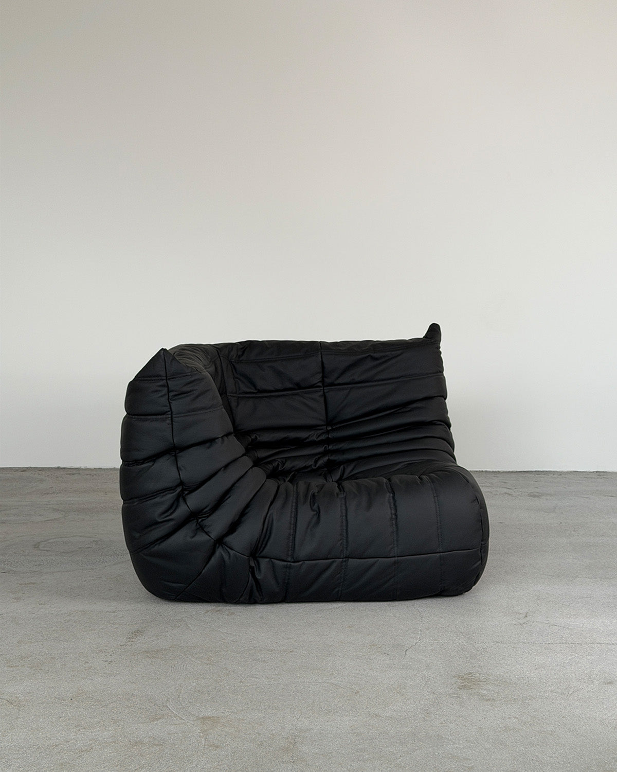 A black leather corner Togo lounge chair by Michel Ducaroy for Ligne Roset, shown on a plain background.