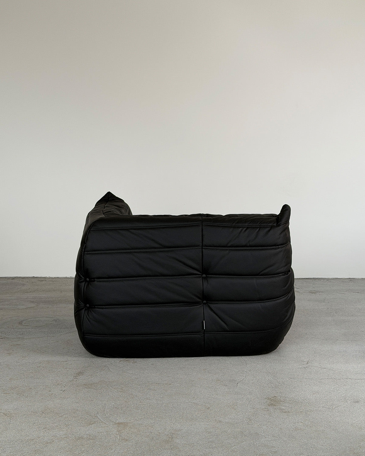 A black leather corner Togo lounge chair by Michel Ducaroy for Ligne Roset, shown on a plain background.