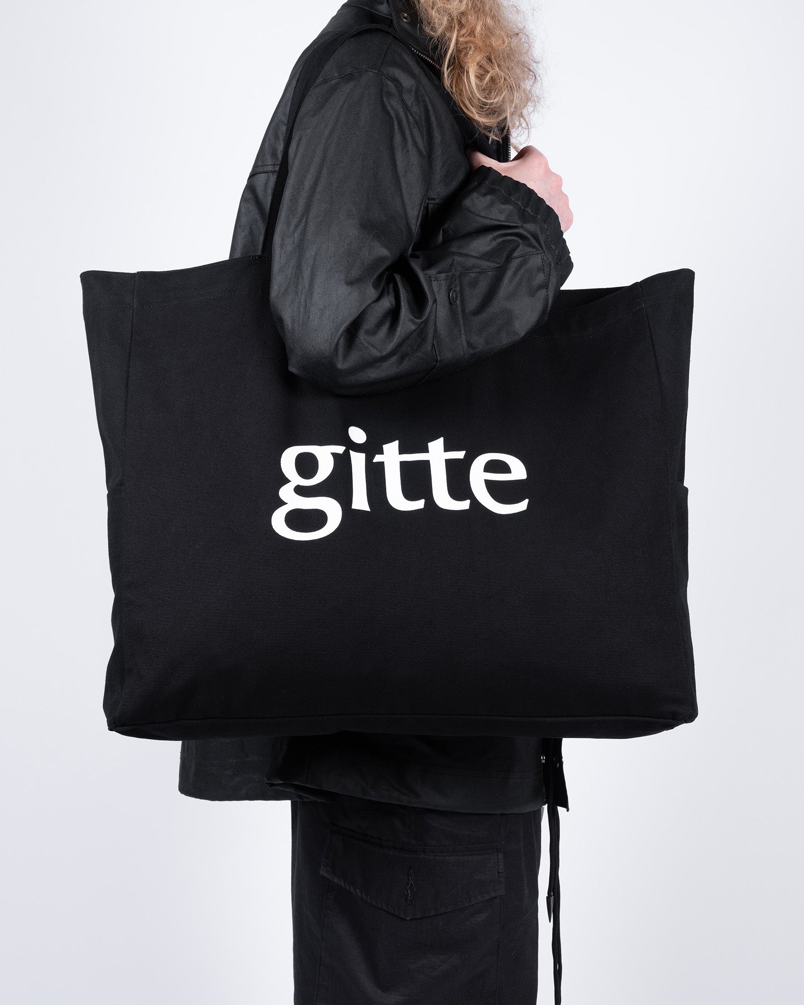 Person holding a black tote bag with 'gitte' printed on it against a white background