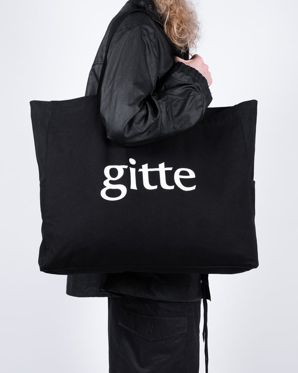 Person holding a black tote bag with 'gitte' printed on it against a white background