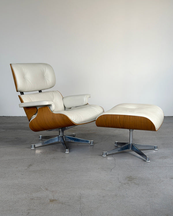 Mid-century modern Vitra Cream Eames Lounge Chair and Ottoman by Charles & Ray Eames, featuring cream leather upholstery and curved wood veneer shells on a metal swivel base, photographed in a minimalist studio setting.